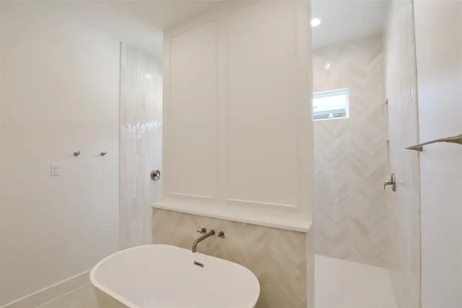 The spacious freestanding tub is paired with a sleek quartz ledge to hold your essentials, while the wall above, accented in harmony with the tile and vanity, serves as a masterful showcase of craftsmanship creating a serene, spa-like experience. The spacious freestanding tub is paired with a sleek quartz ledge to hold your essentials, while the wall above, accented in harmony with the tile and vanity, serves as a masterful showcase of craftsmanship creating a serene, spa-like experience.