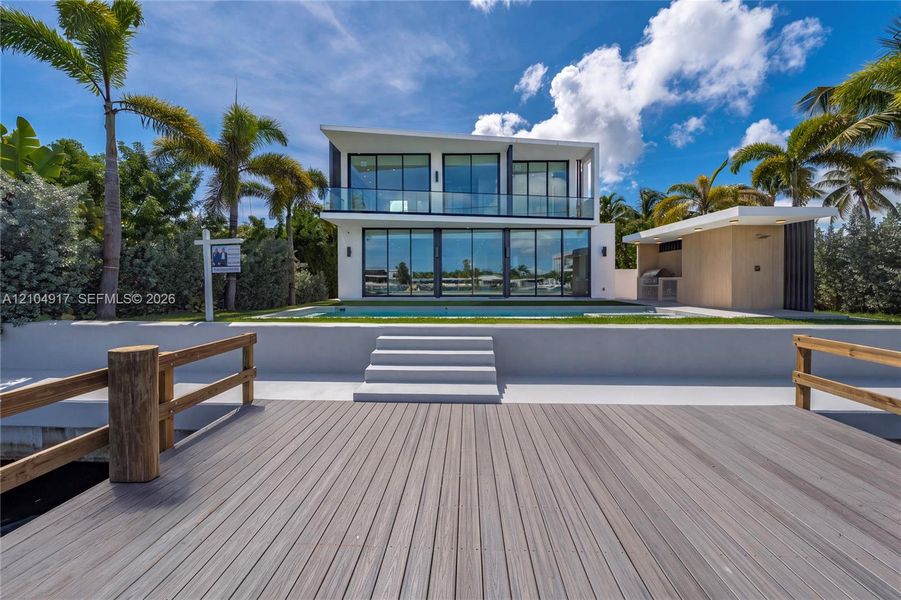 Modern waterfront residence featuring a multi-level structure with floor-to-ceiling glass paneling, a private dock, an integrated swimming pool, and an outdoor kitchen structure