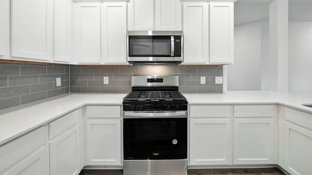Kitchen featuring appliances with stainless steel finishes, white cabinets, decorative backsplash, and light stone counters Kitchen featuring appliances with stainless steel finishes, white cabinets, decorative backsplash, and light stone counters