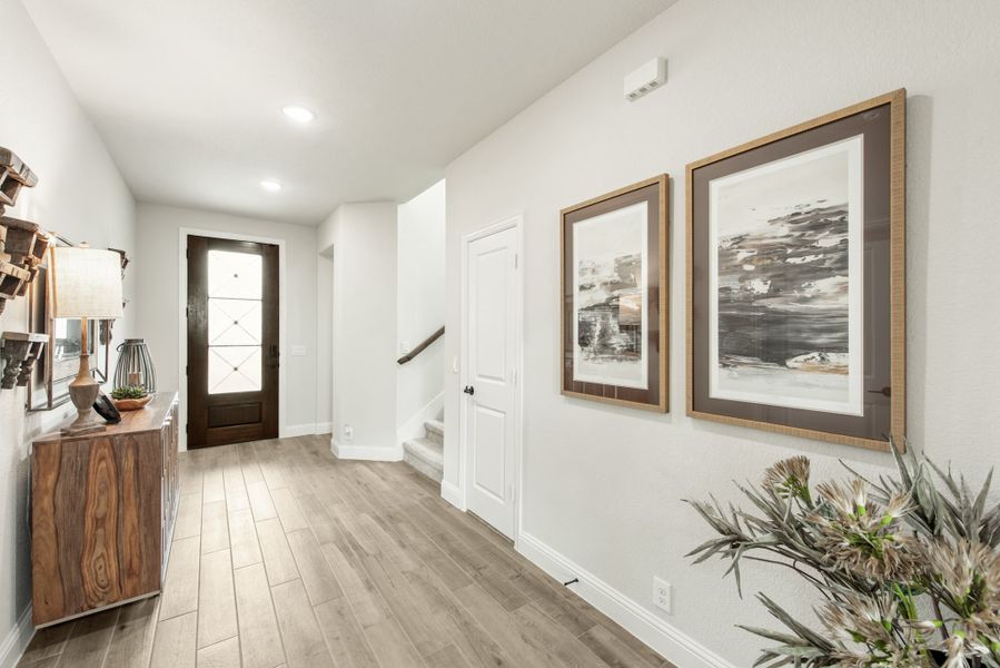 Entryway foyer with dark wood front door, hardwood floors, staircase, and framed wall art