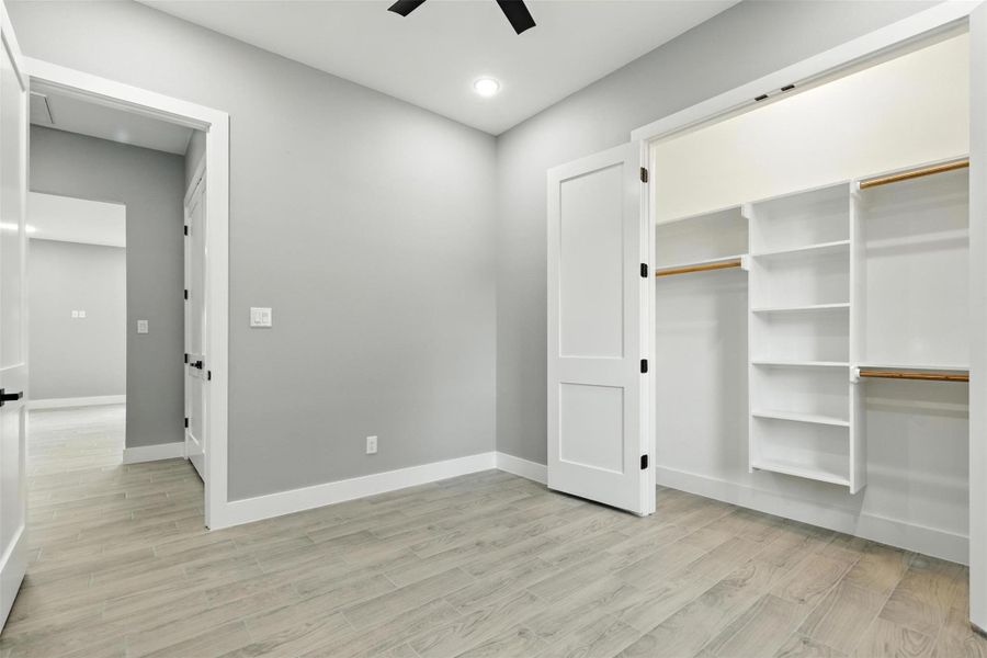 This photo shows a bright, modern closet with light flooring and neutral gray walls. It features built-in shelving and hanging space, with white doors and trim for a clean, sleek look.