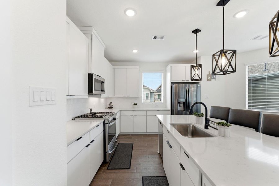 Designer kitchen featuring sleek quartz countertops, crisp white cabinetry, stainless steel appliances, and a spacious layout perfect for everyday cooking or entertaining.