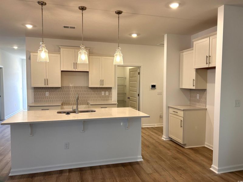 Kitchen with backsplash, a breakfast bar area, decorative light fixtures, light stone counters, and a center island with sink
