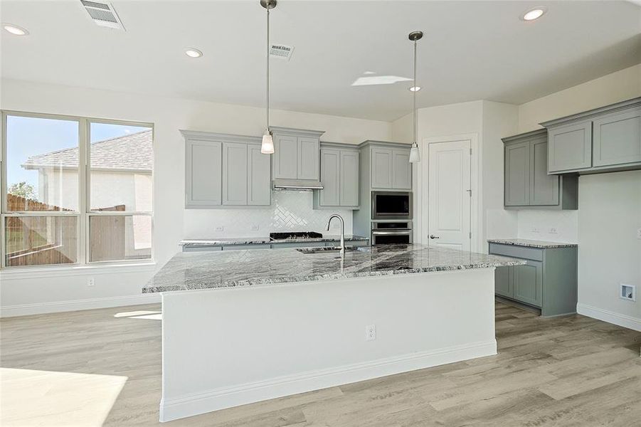 Kitchen with stone counters, sink, light hardwood / wood-style floors, stainless steel appliances, and pendant lighting