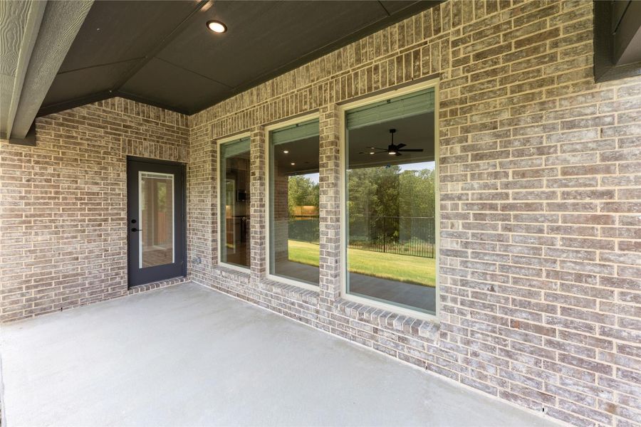 Covered back patio with brick exterior, large windows, and concrete floor with recessed lighting overhead Covered back patio with brick exterior, large windows, and concrete floor with recessed lighting overhead