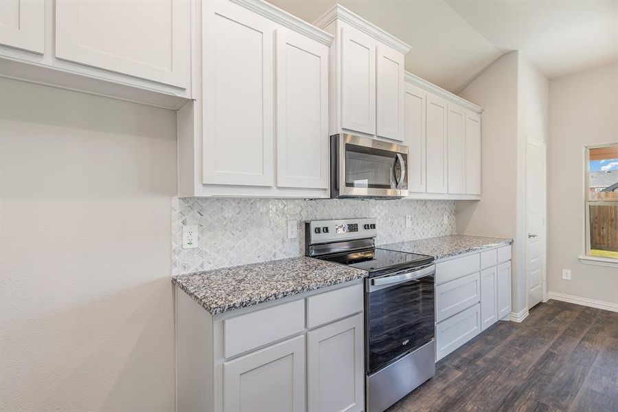 Kitchen with white cabinetry, light stone countertops, dark wood-type flooring, stainless steel appliances, and backsplash