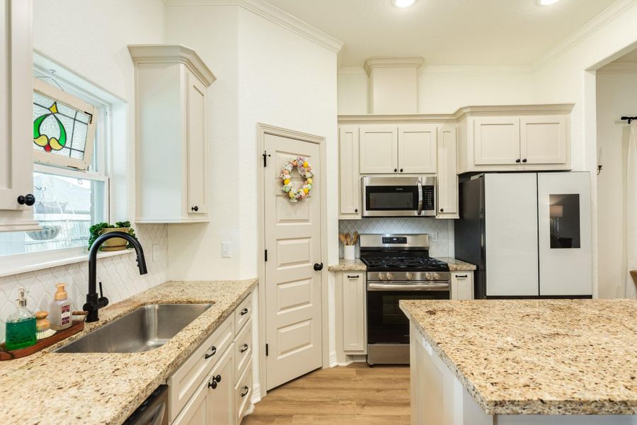 This kitchen features elegant granite countertops and white cabinetry, complemented by stainless steel appliances. The space is well-lit and includes a charming stained glass window, providing a blend of functionality and style.