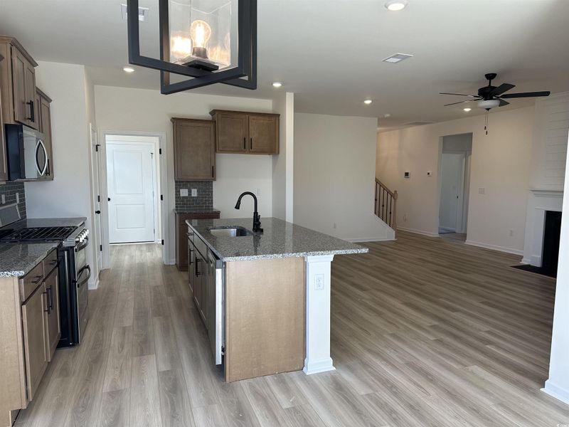 Kitchen featuring dark stone counters, appliances with stainless steel finishes, a fireplace with flush hearth, backsplash, and ceiling fan