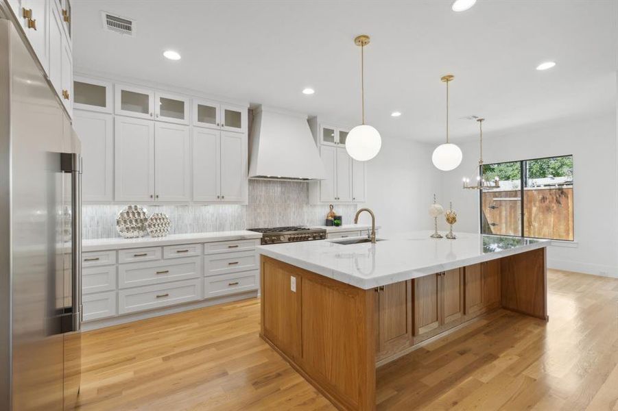 Kitchen with white cabinets, appliances with stainless steel finishes, a kitchen island with sink, and custom exhaust hood