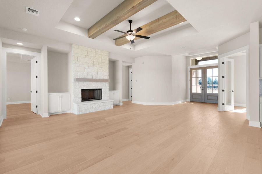 Unfurnished living room featuring french doors, a raised ceiling, light wood-type flooring, ceiling fan, and a stone fireplace