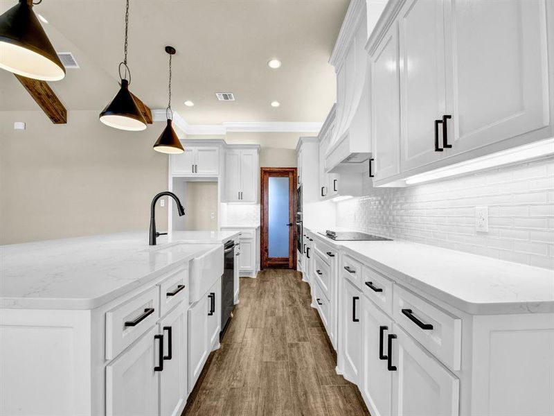 Kitchen featuring black appliances, beamed ceiling, light stone counters, white cabinetry, and decorative light fixtures