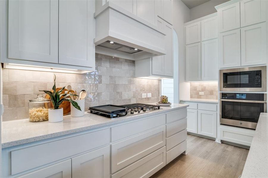 Kitchen featuring white cabinetry, premium range hood, backsplash, appliances with stainless steel finishes, and light wood-type flooring