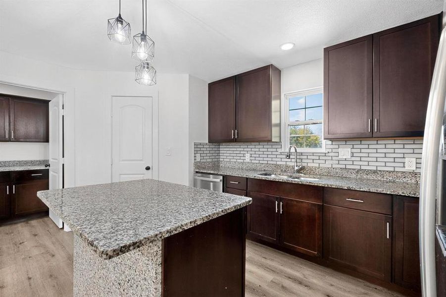Kitchen featuring dark brown cabinetry, light stone countertops, a center island, light wood finished floors, and recessed lighting
