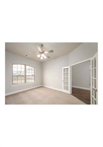 Carpeted spare room featuring ceiling fan and french doors