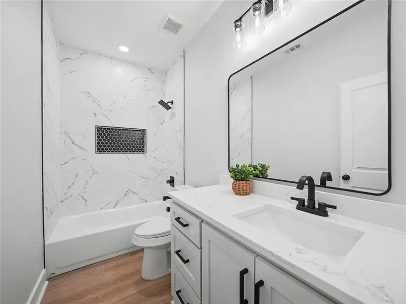 Bathroom featuring a white bathtub with a tile surround, black hexagonal tile shower niche, and matte black fixtures Bathroom featuring a white bathtub with a tile surround, black hexagonal tile shower niche, and matte black fixtures