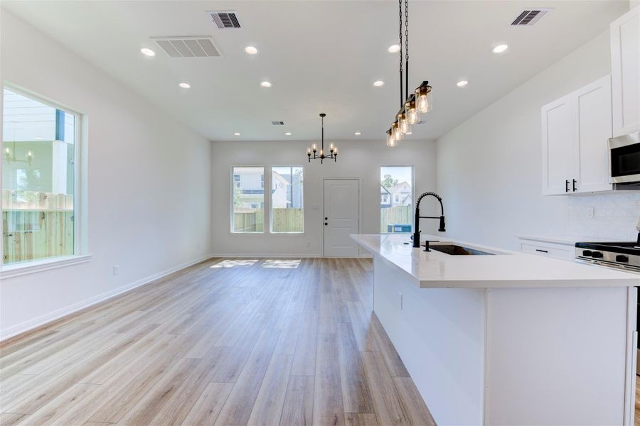 Open-concept living with a quartz island, deep single-basin sink, and matte black faucet. White cabinetry, subway tile backsplash, and stainless appliances keep a clean look, while LVP flooring, recessed lighting, and pendant fixtures complete the space.