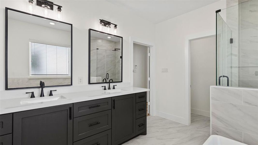 This modern bathroom features a double vanity with sleek black fixtures, large mirrors, and ample storage. The space is bright and airy with light-colored tile flooring and a glass-enclosed shower.