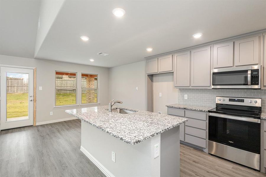 Kitchen featuring sink, decorative backsplash, an island with sink, appliances with stainless steel finishes, and light stone counters