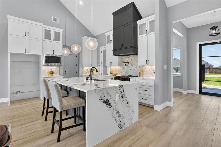 Contemporary kitchen featuring an oversized waterfall island with seating, a distinctive black vent hood, stainless steel appliances, and wood-finish flooring