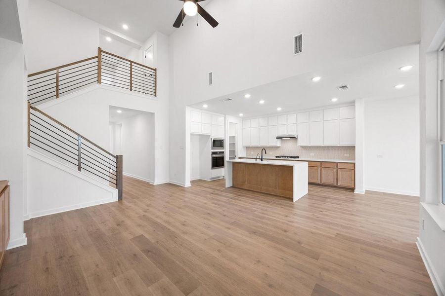 Unfurnished living room with a towering ceiling, light wood-style flooring, recessed lighting, ceiling fan, and stairway Unfurnished living room with a towering ceiling, light wood-style flooring, recessed lighting, ceiling fan, and stairway