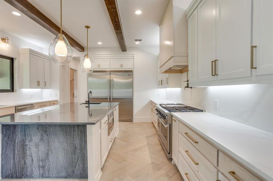 Kitchen with light stone countertops, high quality appliances, white cabinetry, parquet flooring, and beamed ceiling