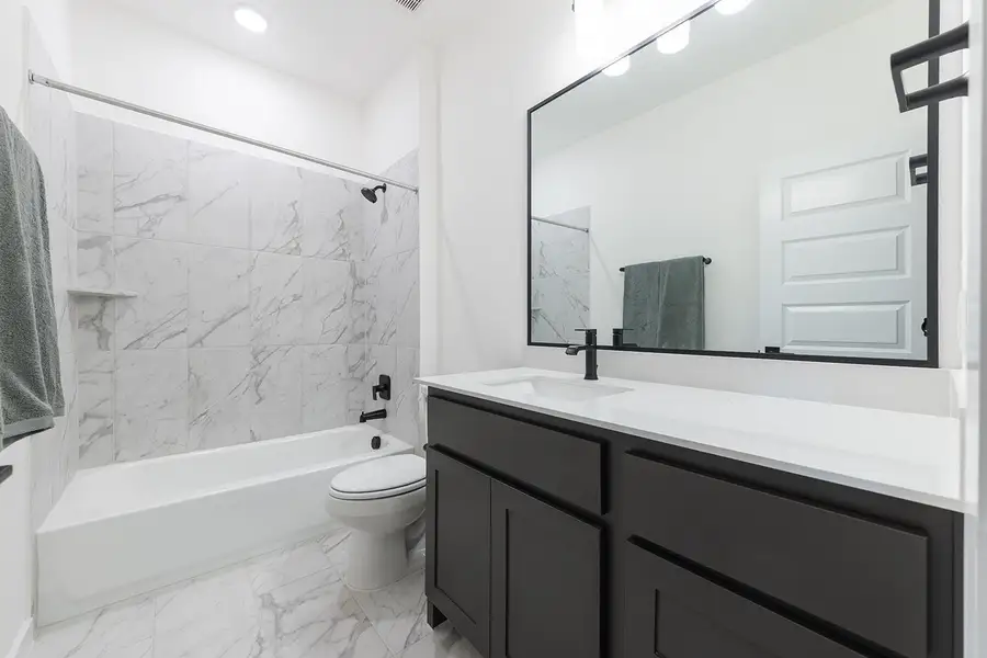 Guest bathroom with shower/bathtub combination, light marble finish floors, and vanity