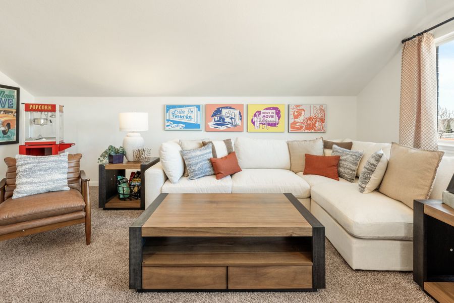 Bonus room with white sectional sofa, wood coffee table, and drive-in movie themed wall art on carpet