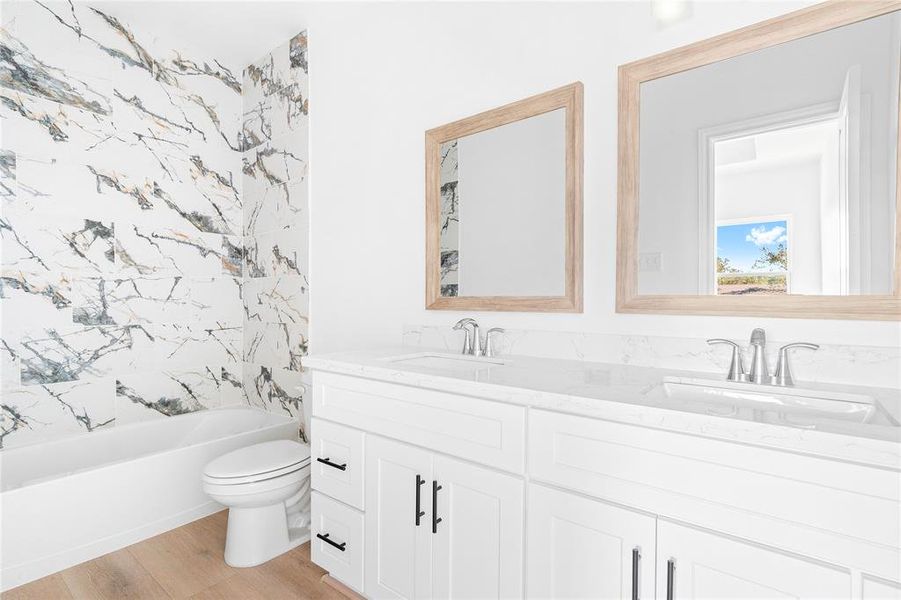 The master bathroom exudes modern style with quartz countertops, dual sinks, individual mirrors, white cabinets, and a shower-tub combo. (Photo may be enhanced)