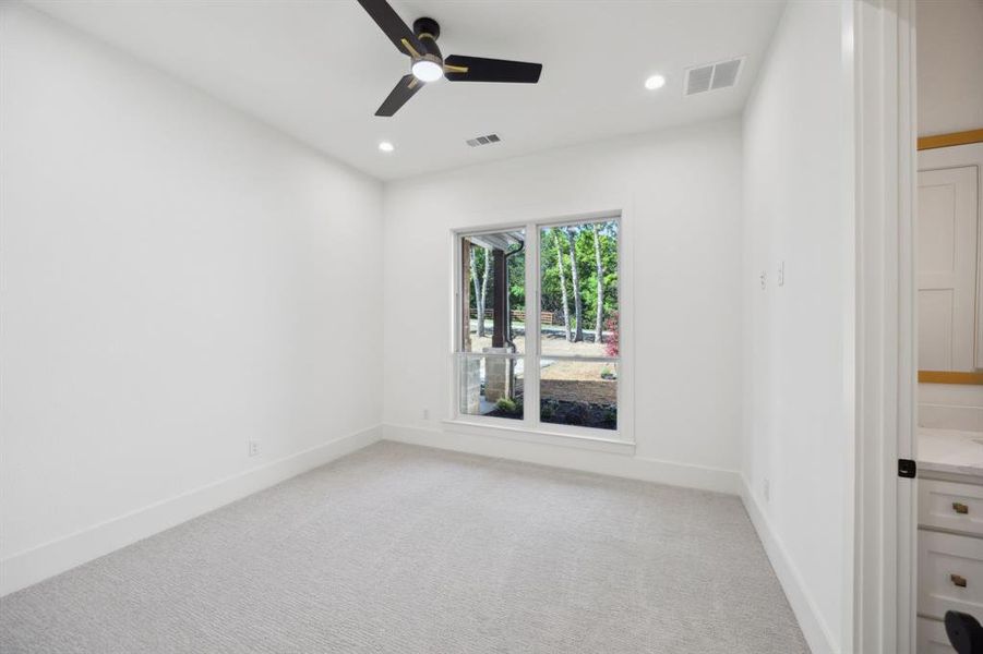 Downstairs bedroom featuring visible vents, ceiling fan, light colored carpet, and baseboards Downstairs bedroom featuring visible vents, ceiling fan, light colored carpet, and baseboards