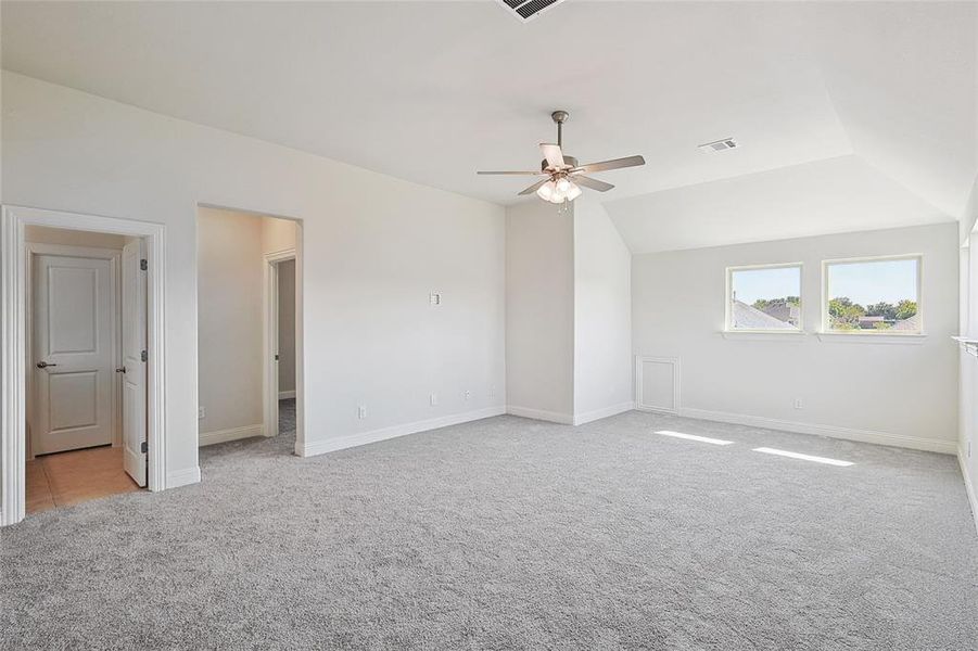 Carpeted spare room featuring vaulted ceiling and ceiling fan