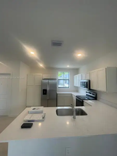 Kitchen featuring white shaker-style cabinetry, quartz countertops, a peninsula with an undermount stainless steel sink, and recessed lighting
