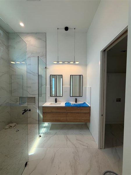 Bathroom with a marble finish shower, double vanity, light marble finish flooring, and recessed lighting