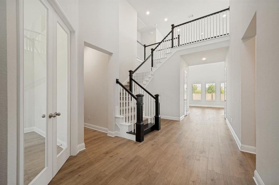 Grand entryway with wood-finish flooring, a two-story staircase featuring black newel posts and handrails, white balusters, recessed lighting, and white baseboards