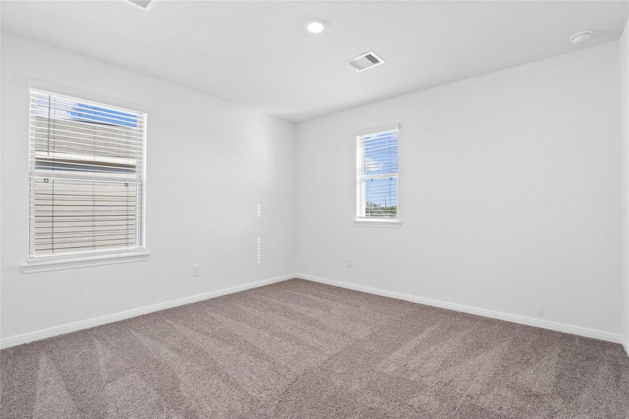 This secondary bedroom offers comfort and style with plush carpeting, neutral paint tones, recessed lighting, a large window with blinds, and a generously sized closet.