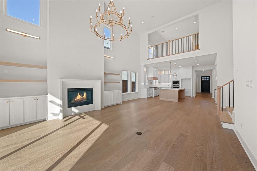 Unfurnished living room featuring a glass covered fireplace, light wood-style floors, a chandelier, a high ceiling, and recessed lighting Unfurnished living room featuring a glass covered fireplace, light wood-style floors, a chandelier, a high ceiling, and recessed lighting