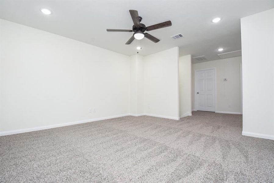 Mater bedroom downstairs with beige carpet, white walls, ceiling fan, recessed lighting, and a closed door. Clean and unoccupied space.