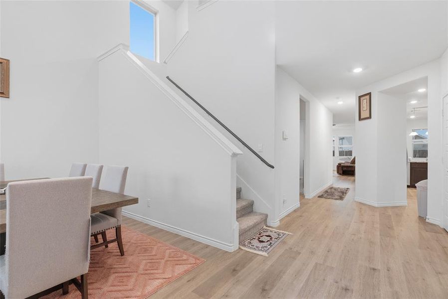 Bright interior with light wood-finish flooring extending throughout, a carpeted staircase with a dark handrail, and high ceilings