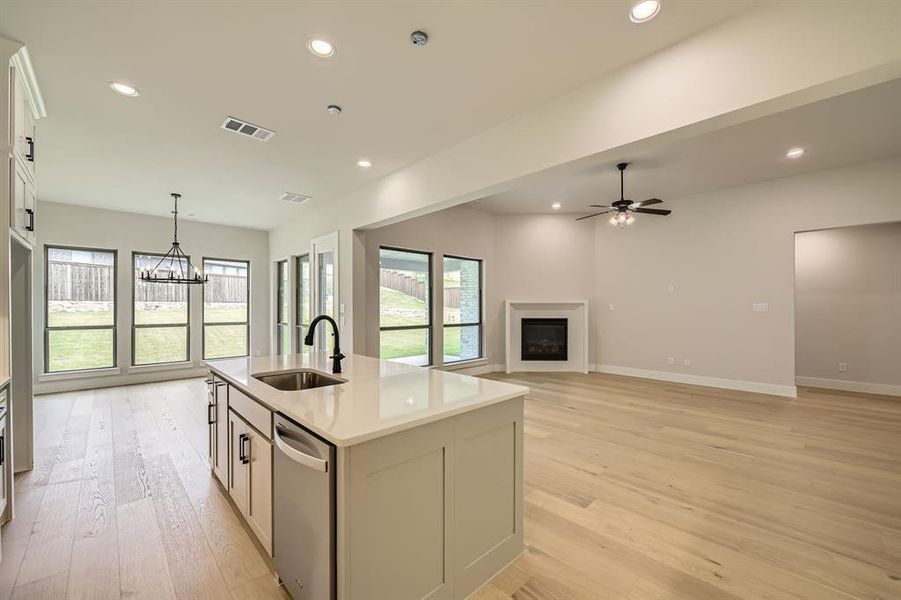 Kitchen featuring stainless steel dishwasher, light wood finished floors, a fireplace, an island with sink, and light countertops Kitchen featuring stainless steel dishwasher, light wood finished floors, a fireplace, an island with sink, and light countertops