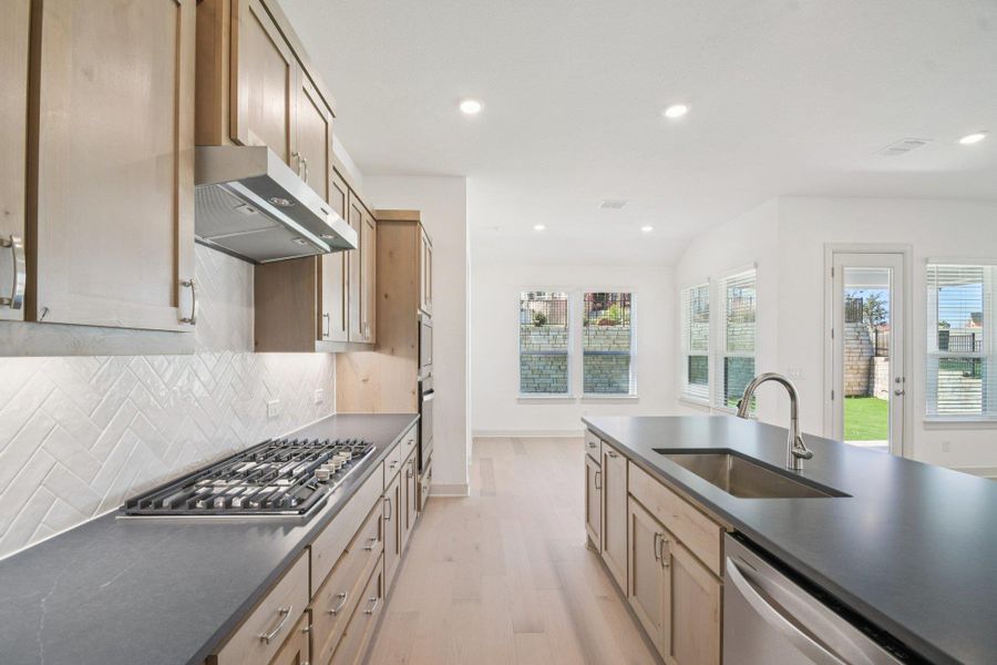 Kitchen featuring light wood-type flooring, recessed lighting, stainless steel appliances, under cabinet range hood, and light brown cabinetry Kitchen featuring light wood-type flooring, recessed lighting, stainless steel appliances, under cabinet range hood, and light brown cabinetry