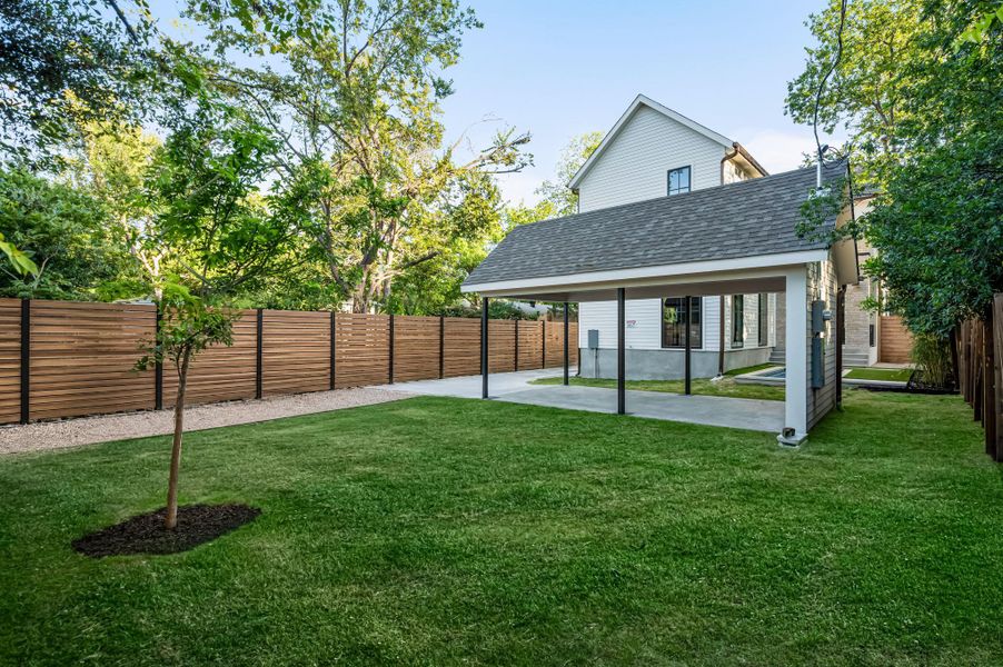 A verdant backyard with a stylish modern fence, a young tree, and a practical carport.