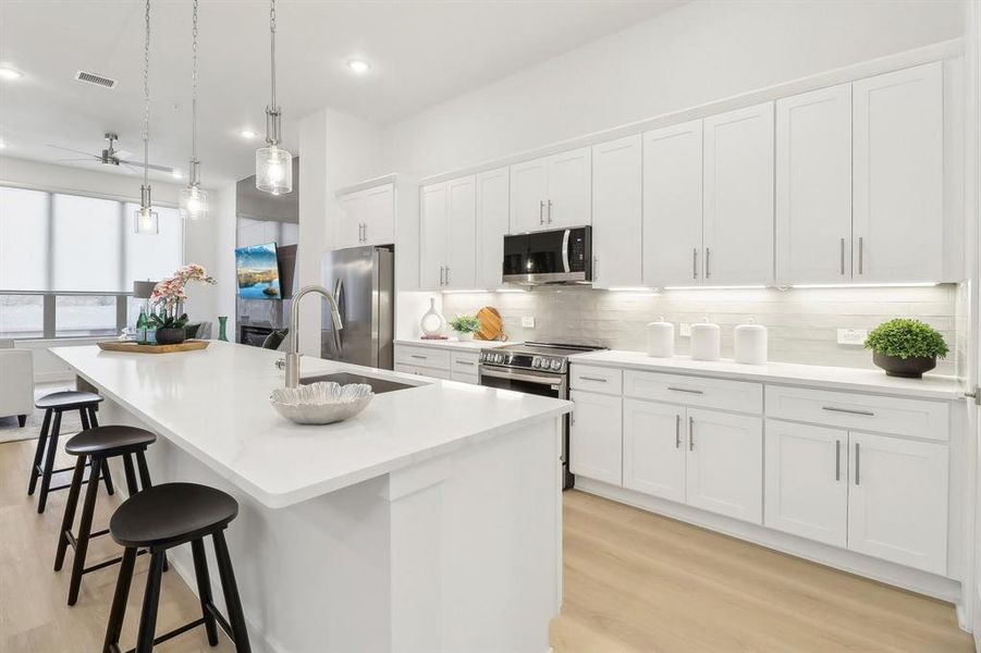 Kitchen with a center island with sink, stainless steel appliances, visible vents, decorative backsplash, and white cabinets