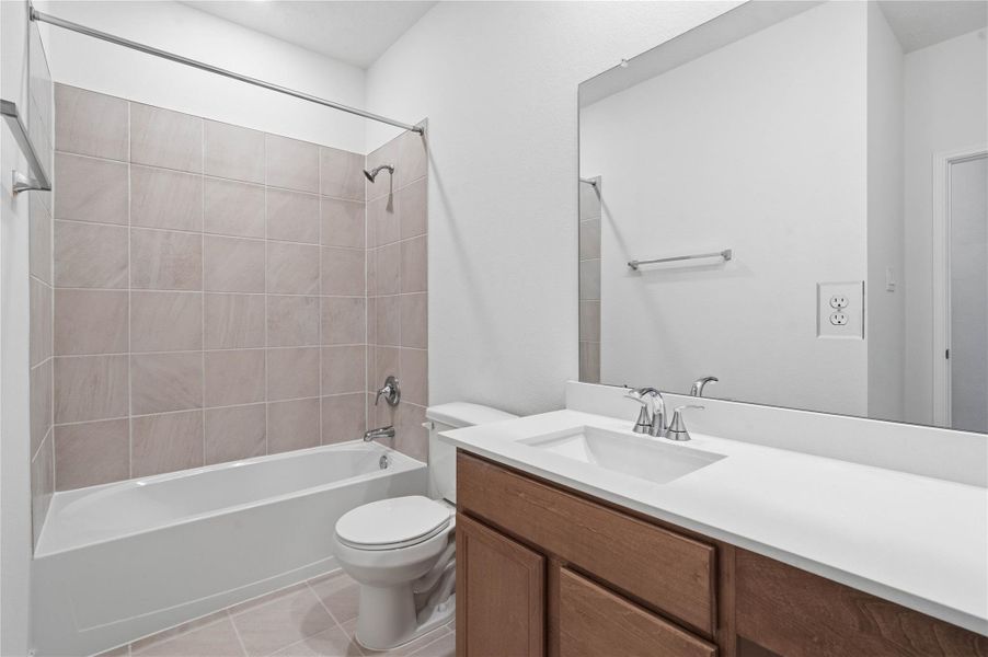 The secondary bathroom offers tile flooring, a bath/shower combination with a stylish tile surround, rich stained wood cabinetry with added knee space and elegant light countertops, a mirror, and sleek fixtures with modern finishes. The secondary bathroom offers tile flooring, a bath/shower combination with a stylish tile surround, rich stained wood cabinetry with added knee space and elegant light countertops, a mirror, and sleek fixtures with modern finishes.