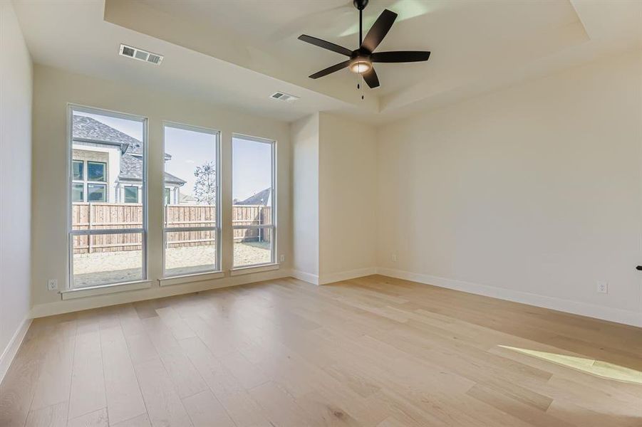Empty room featuring a raised ceiling, light wood-type flooring, and a ceiling fan
