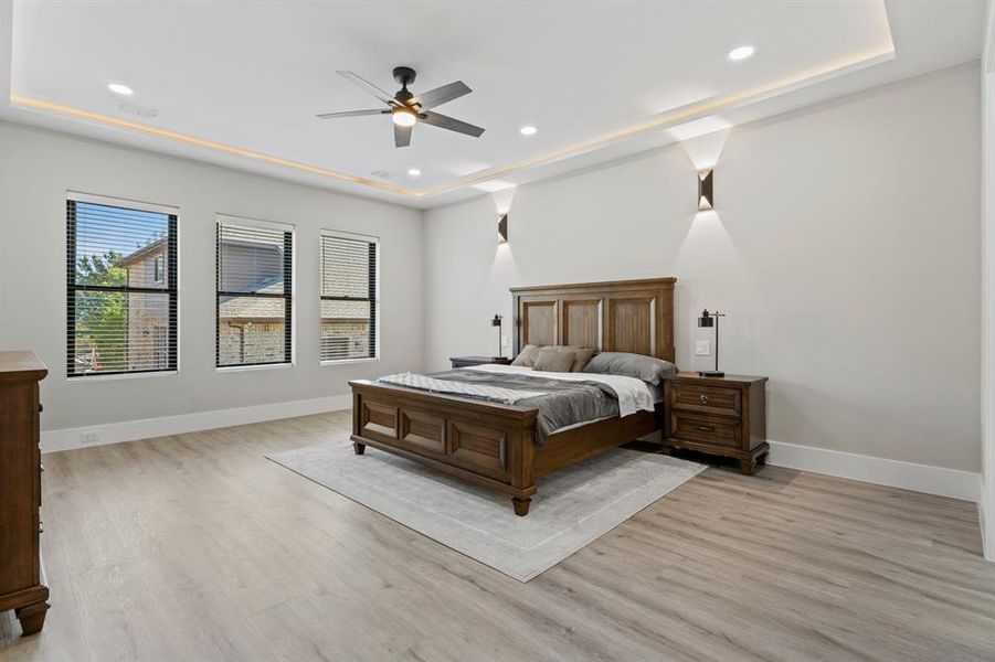 Bedroom with light wood-style floors, ceiling fan, recessed lighting, and a tray ceiling