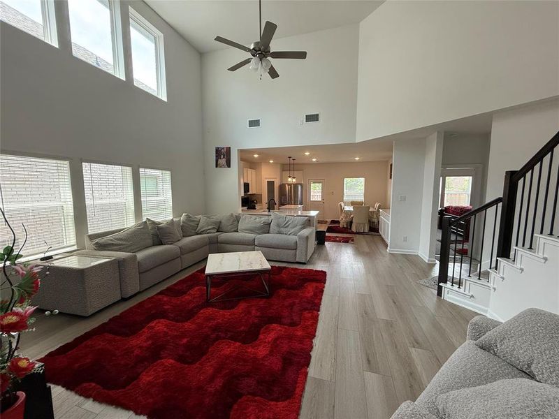 Soaring ceilings with upper windows, wood-finish flooring, and a contemporary ceiling fan