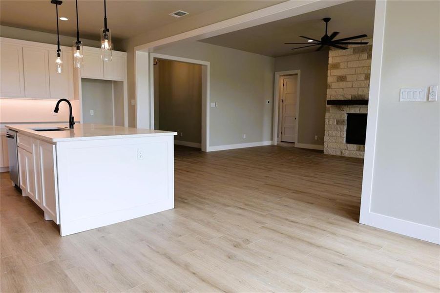 Kitchen with pendant lighting, ceiling fan, light hardwood / wood-style floors, a stone fireplace, and sink