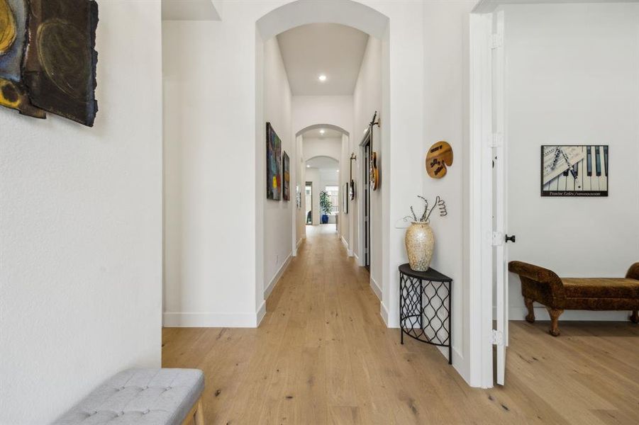 Hall with arched walkways, light wood-style flooring, recessed lighting, and baseboards