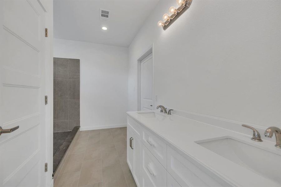 Full bathroom with double vanity, recessed lighting, light tile patterned flooring, and tiled shower