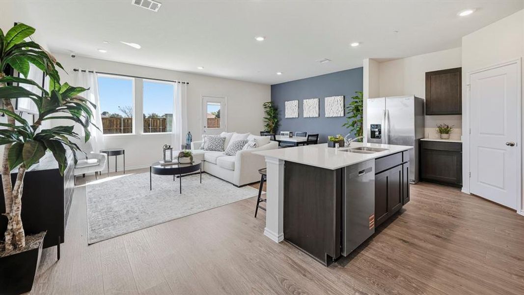 Kitchen with a center island with sink, open floor plan, dark brown cabinets, light wood finished floors, and stainless steel appliances Kitchen with a center island with sink, open floor plan, dark brown cabinets, light wood finished floors, and stainless steel appliances