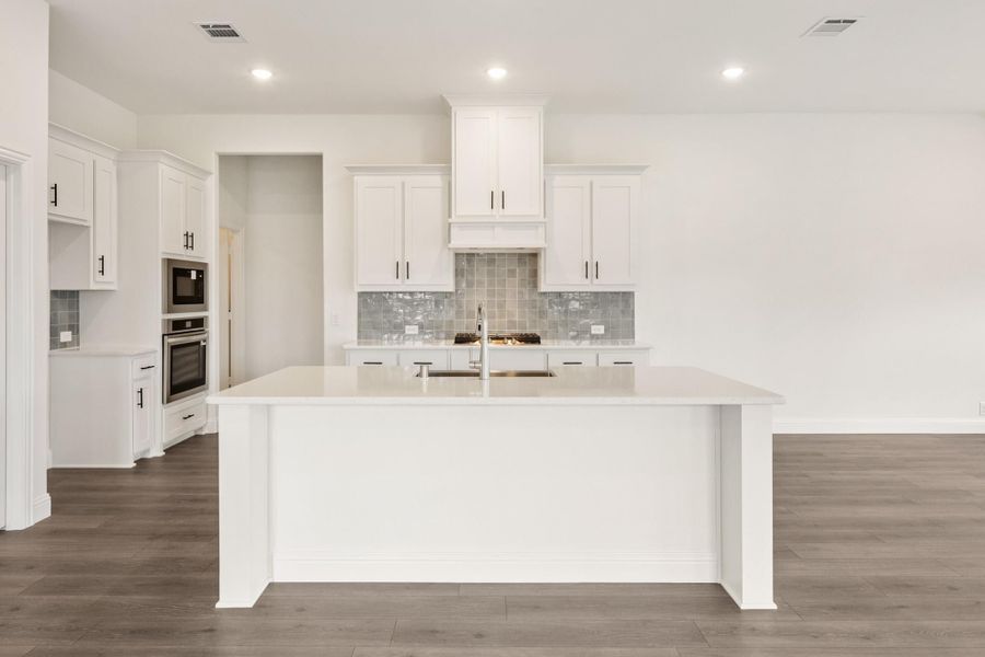 White kitchen with large center island, gray tile backsplash, stainless steel appliances, and dark hardwood floors